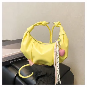 Close-up of a bright yellow hobo crescent bag with a knotted handle and heart charm