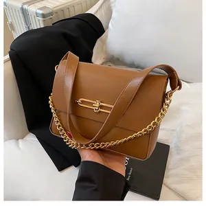 Detail of a brown leather shoulder bag featuring a gold H-shaped lock and chain strap