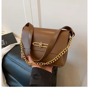 Detail of a brown shoulder bag with a gold H-shaped clasp and thick metal chain