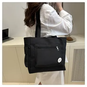 Detail of black canvas tote bag showing the front zipper pocket and good luck badge