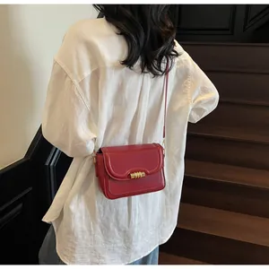 Detail view of retro red leather crossbody bag with a distinctive golden cylinder lock buckle