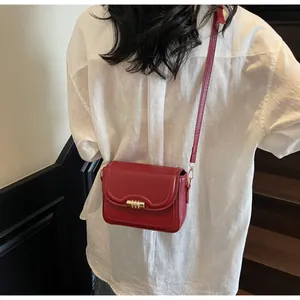 Close-up of a red leather crossbody bag with a gold cylindrical buckle on a white shirt