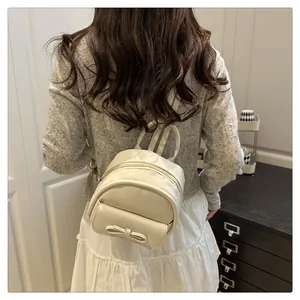 Close-up of a mini cream leather backpack with bow detail worn by a model in a cozy room