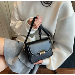 Detail of black PU leather crossbody bag featuring wave flap and gold cylinder clasp