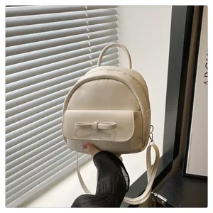 Close-up of cream mini backpack featuring a decorative bow flap and sleek faux leather finish
