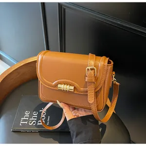 Detail of caramel brown leather crossbody bag featuring a golden cylindrical lock on stool