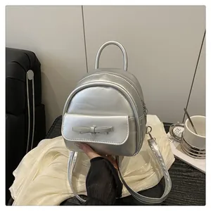 Silver mini backpack with metallic finish and bow detail held in a modern setting