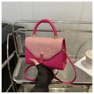 Close-up of pink crossbody bag with red and white V-patterned flap and gold metal clasp