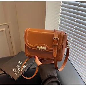 Detail of a brown PU leather crossbody bag with a unique gold cylindrical metal buckle
