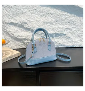 Sky blue shell bag with double gold zippers and detachable strap on black wooden surface