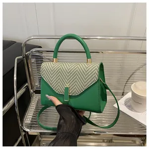 Close-up of green leather handbag with herringbone fabric flap and gold buckle hardware