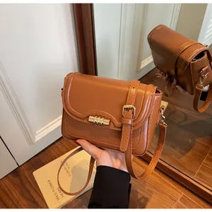 Detail view of brown faux leather crossbody bag with golden metal lock and strap details