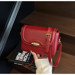Detail of red PU leather shoulder bag featuring a unique shaped flap and gold metal clasp