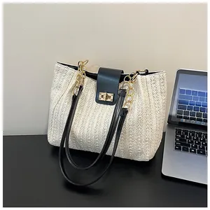 Détail du cabas tissé beige montrant la sangle en cuir noir et le fermoir doré rotatif