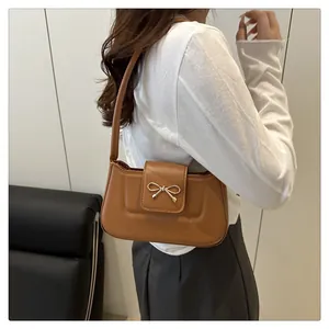 Sac baguette marron en similicuir avec boucle nœud doré porté à l'épaule par un mannequin