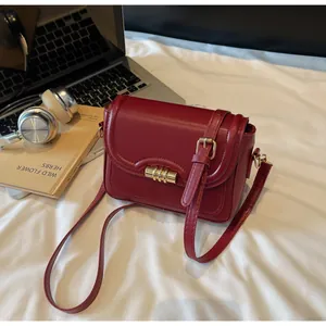 Detail of burgundy PU leather crossbody bag with gold twist lock on a white surface