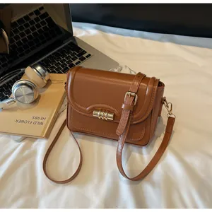 Close-up of brown PU leather shoulder bag with gold cylindrical lock on white desk
