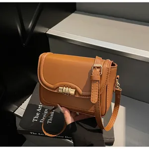 Close-up of caramel PU leather crossbody bag with elegant gold bar clasp on a design book