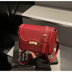 Detail of red leather crossbody bag with gold cylindrical clasp and adjustable strap