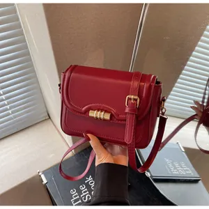 Detail of burgundy PU leather crossbody bag with golden triple-ring buckle and stitching