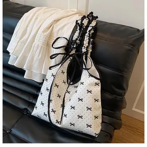 Detail of canvas tote bag with black polka dot bow and ruffled handles on black leather sofa