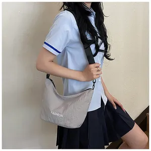 Model wearing a light grey nylon half-moon crossbody bag with black adjustable strap