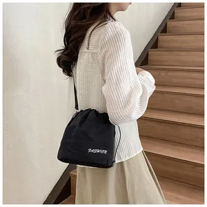 Detail of a black nylon drawstring bucket bag with white fashion lettering and shoulder strap