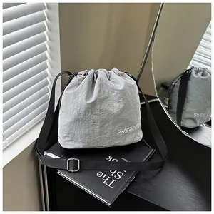 Detail of light grey nylon drawstring bucket bag with fashion text and black wide strap