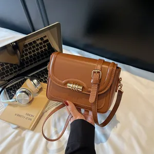 Brown PU leather crossbody bag with gold buckle on a stylish office desk setup