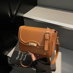 Minimalist brown PU leather crossbody bag with gold buckle on dark stairs background