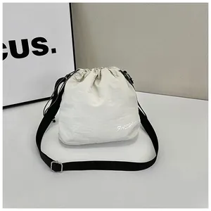 Macro shot of off-white nylon drawstring bucket bag with black adjustable strap and metal buckle