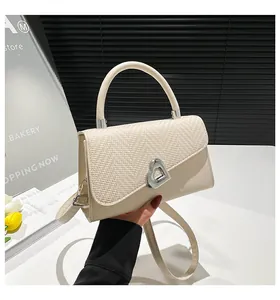 Detail of cream crossbody bag featuring woven texture flap and silver heart buckle