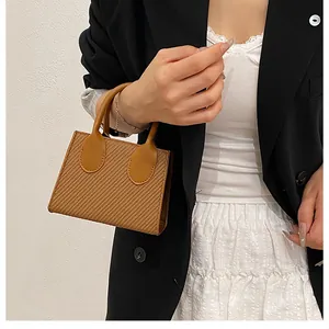 Detailed view of woven straw tote bag with brown leather handles on a model in a black blazer