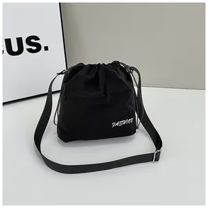 Detail view of black nylon drawstring bucket bag with white FASHION print and strap