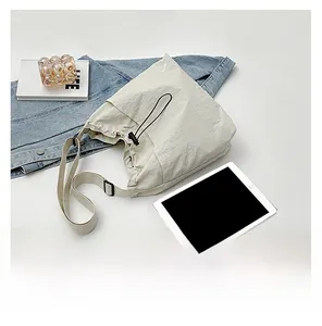 Detail view of beige nylon crossbody bag with drawstring closure and laptop storage