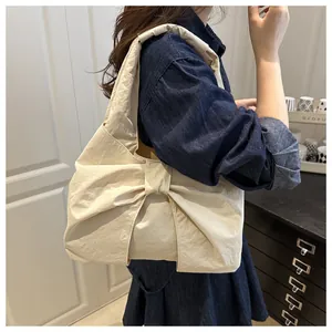 Dettaglio di una borsa beige con grande fiocco e tessuto strutturato su una modella