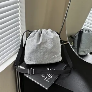 Lightweight grey nylon drawstring bucket bag with adjustable black strap on book