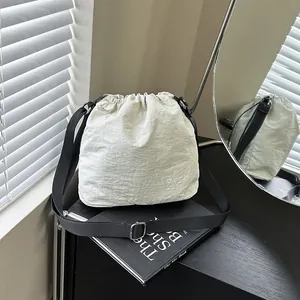 Beige nylon drawstring bucket bag with adjustable black strap and fashion text detail