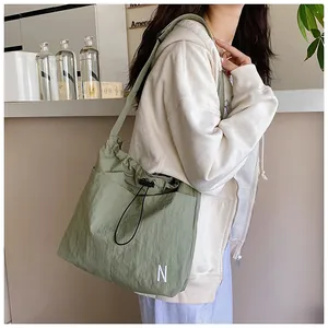 Detail shot of green drawstring crossbody bag featuring white N letter embroidery and texture