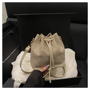 Detailed close-up of beige suede drawstring bucket bag with gold metal buckle and strap