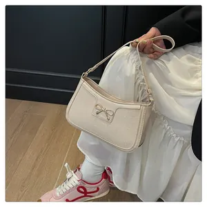 Detail of cream shoulder bag with crocodile texture and gold bow metal decoration