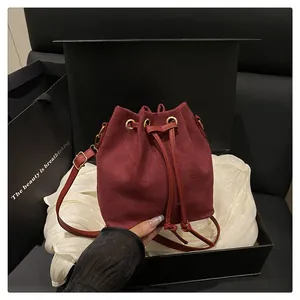 Detail view of burgundy suede bucket bag with gold eyelets and drawstring closure