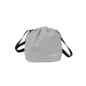 Light grey nylon drawstring bucket bag with a wide black shoulder strap and fashion print