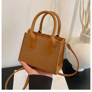 Detail of a brown woven mini crossbody bag with leather handles and textured finish