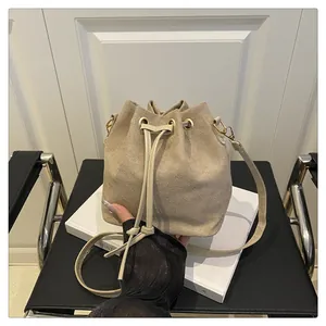 Detail of beige suede drawstring bucket bag with gold eyelets and leather straps