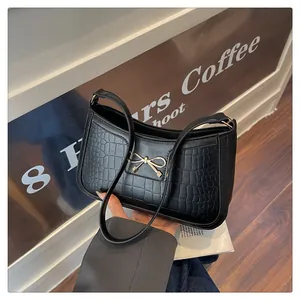 Close-up of black crocodile embossed leather handbag with golden bow metal buckle details