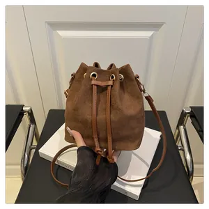 Detail of a brown suede bucket bag featuring a drawstring closure and golden metal eyelets