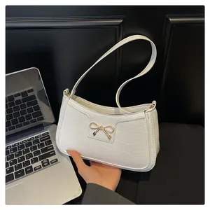 Detail of white crocodile texture underarm bag featuring a gold bow metal buckle