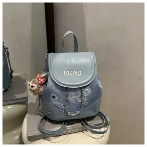 Detail of light blue denim backpack with IBCMB embroidery and plush monkey charm