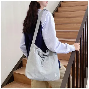 Detail of grey nylon crossbody bag featuring drawstring closure and adjustable wide strap